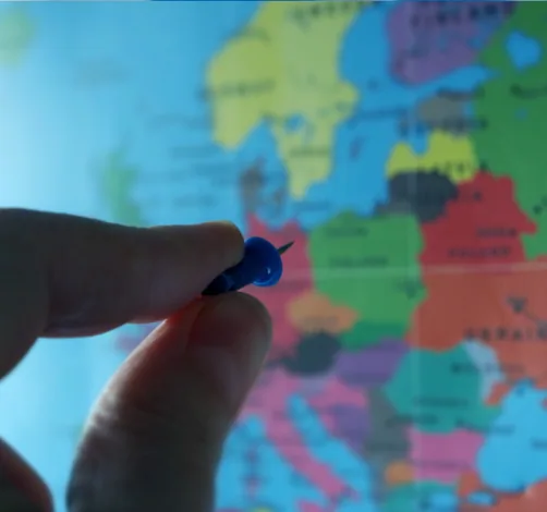 Dłoń wbija pinezkę w mapę Europy